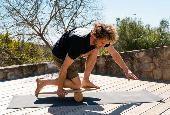Mann beim Surfworkout auf Balance Board aus Holz mit Korkrolle