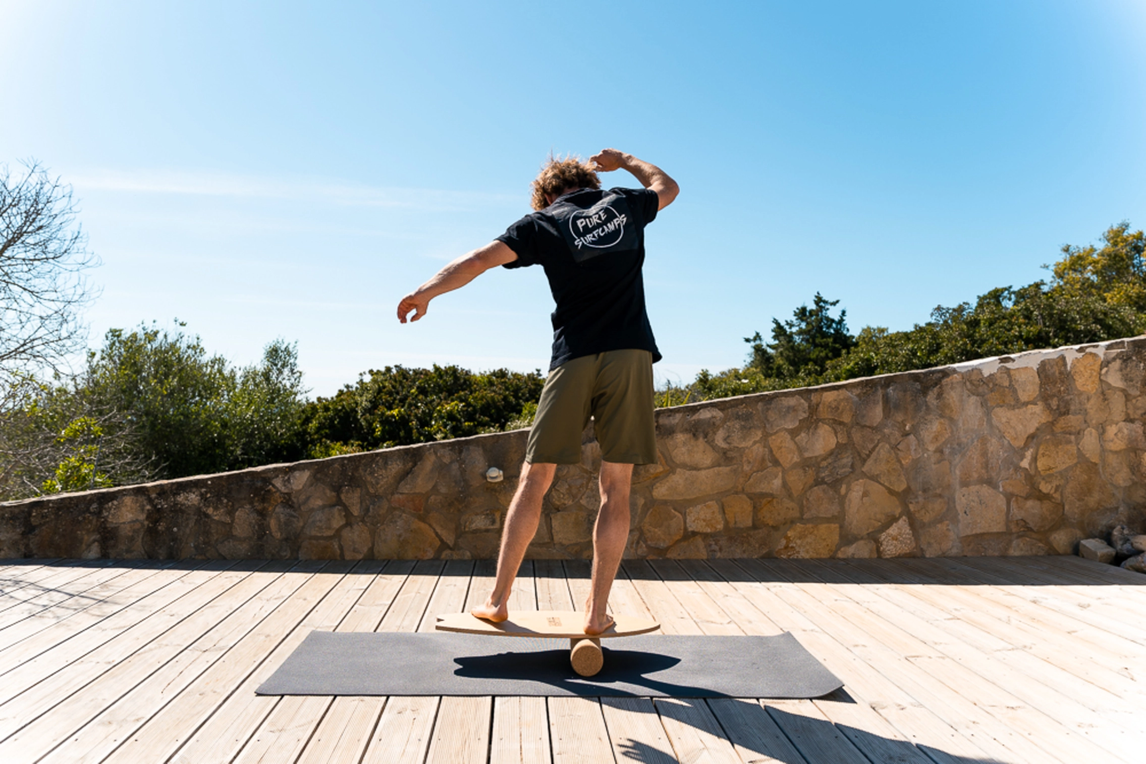 Mann von hinten auf Balance Board aus Holz mit Korkrolle