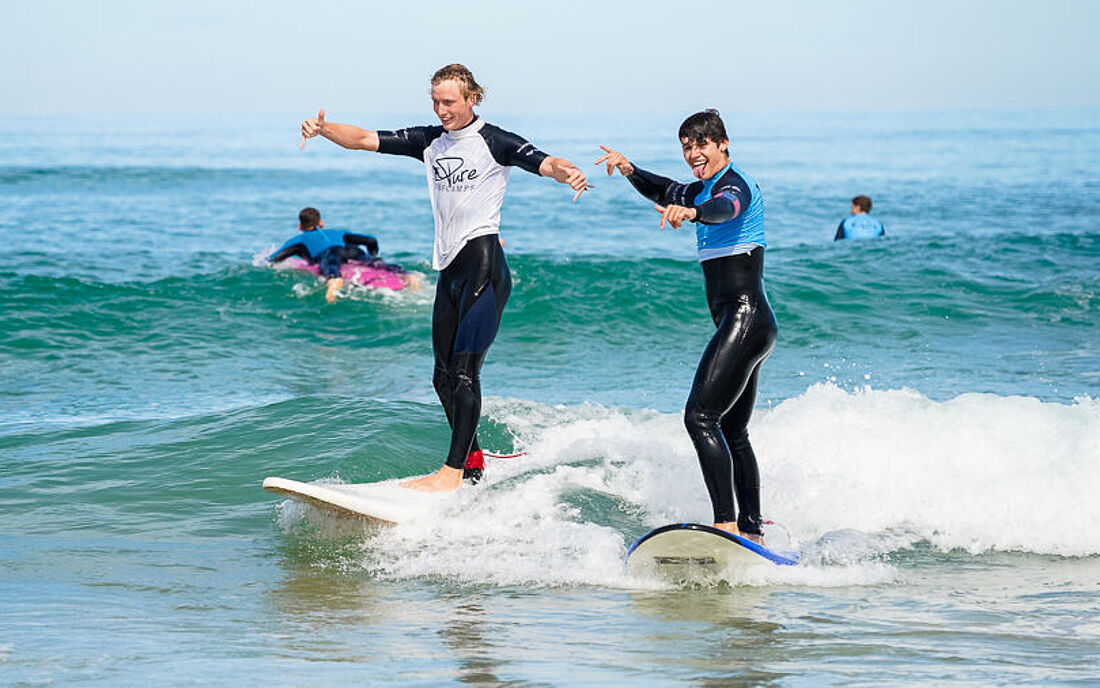 Surflehrer surft gemeinsam mit Surfsch&uuml;ler eine Welle