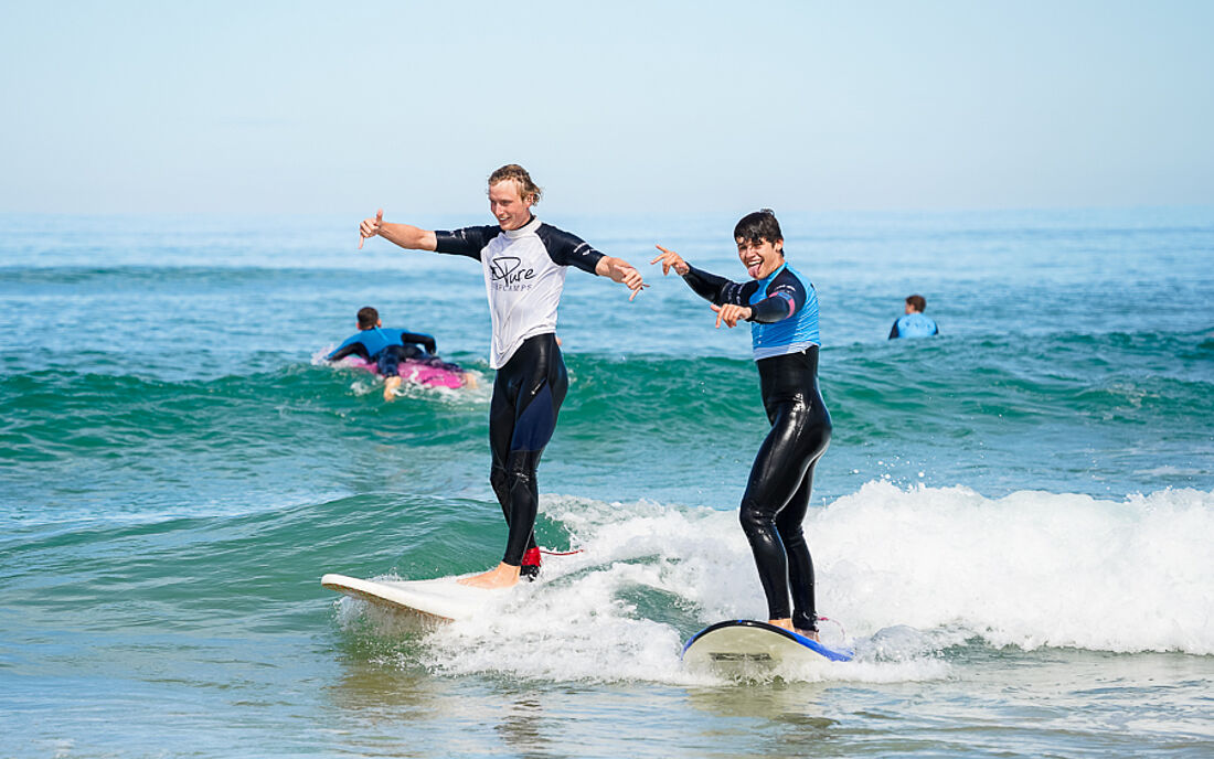 Surflehrer surft gemeinsam mit Surfsch&uuml;ler eine Welle