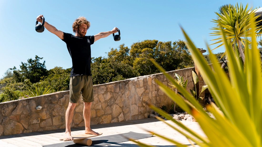 Mann beim Training mit Hanteln auf Balance Board vor Palmen Mann beim Training mit Hanteln auf Balance Board vor Palmen