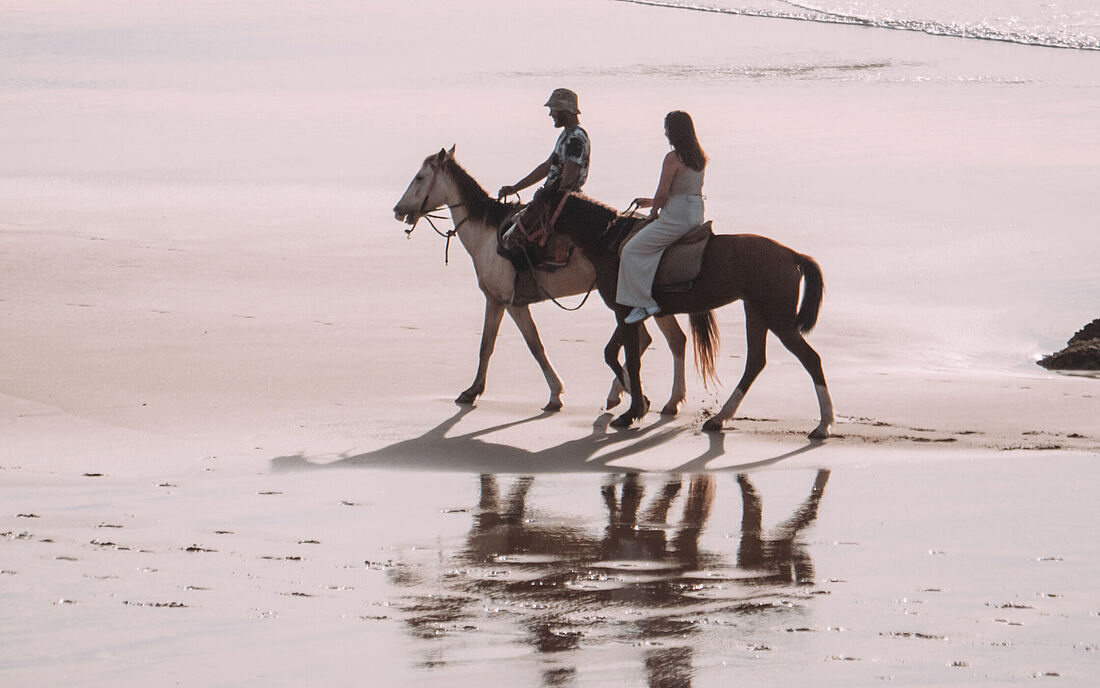 Riding horses along the shore.
