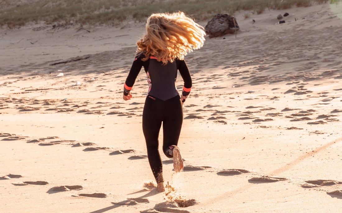 Mädchen läuft im Neoprenanzug am Strand