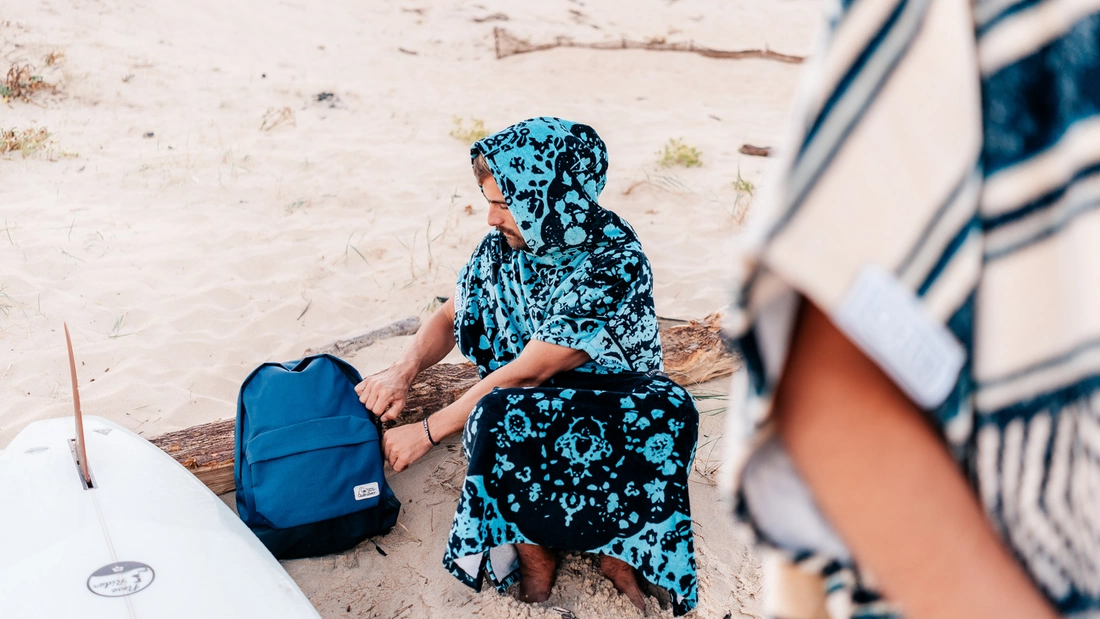 Mann in blau bemustertem Surfponcho am Strand Mann in blau bemustertem Surfponcho am Strand